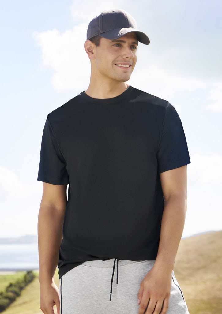 A black men's short sleeve tee worn by a model, paired with grey shorts and a cap in a scenic outdoor setting.