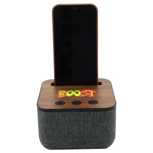 A Bluetooth speaker with a wooden top, grey fabric base, and a slot for a phone. It features buttons on the front and has a logo.