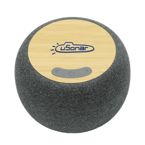 A round wireless speaker with a bamboo top and grey fabric body, featuring buttons for control and a logo.