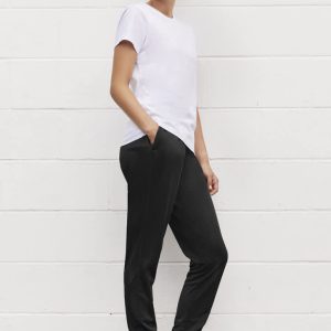 A woman stands in profile wearing a white t-shirt and black track pants with pockets, complemented by black sneakers.