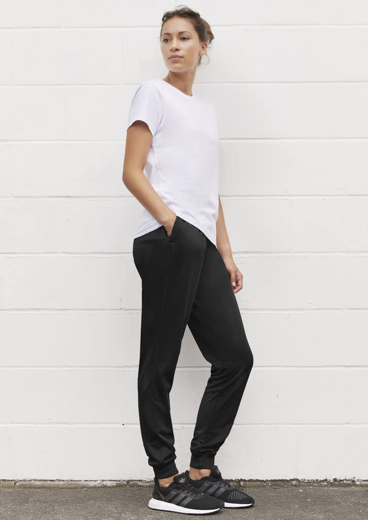 A woman stands in profile wearing a white t-shirt and black track pants with pockets, complemented by black sneakers.