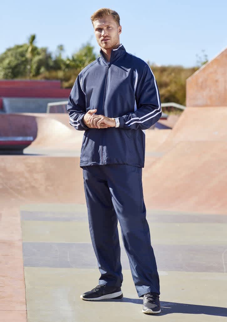 A person stands wearing navy unisex track pants and a matching jacket, set against a skatepark background.