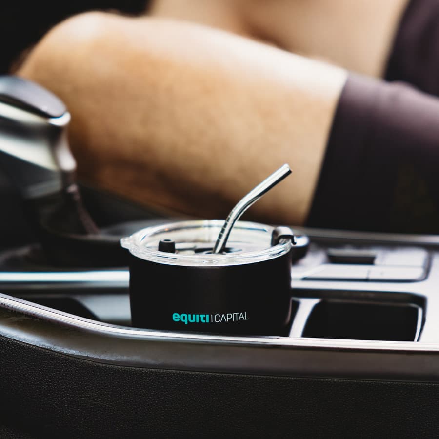 A drink bottle featuring a black design, with a metal straw, placed in a car cup holder. Includes a logo.