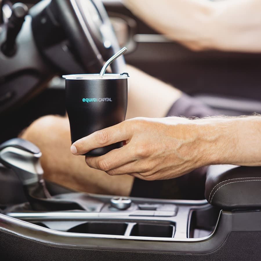 A drink bottle in black with a straw, held inside a vehicle, featuring a logo on the side.