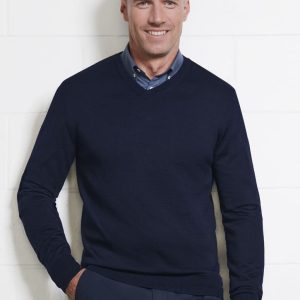 A navy men's knitted pullover with a V-neck, modelled by a smiling man against a white wall.