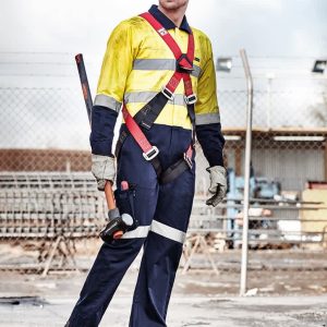 A man in a yellow and navy rugged cooling taped overall with a harness, standing on a construction site.