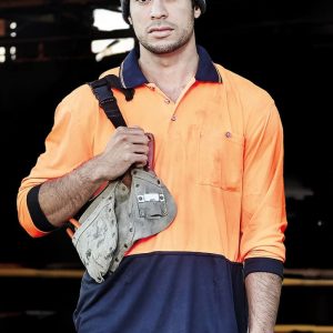 A man wearing an orange and navy blue long sleeve polo shirt, holding a work bag and wearing a grey beanie.