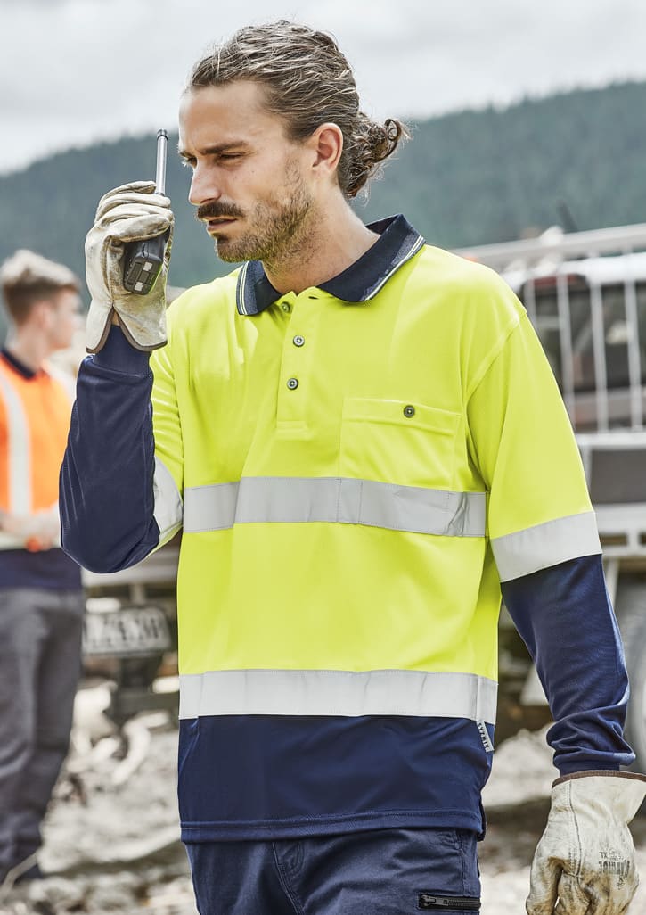 A man wears a bright yellow and navy long sleeve polo with reflective tape, holding a walkie-talkie. It has a logo.