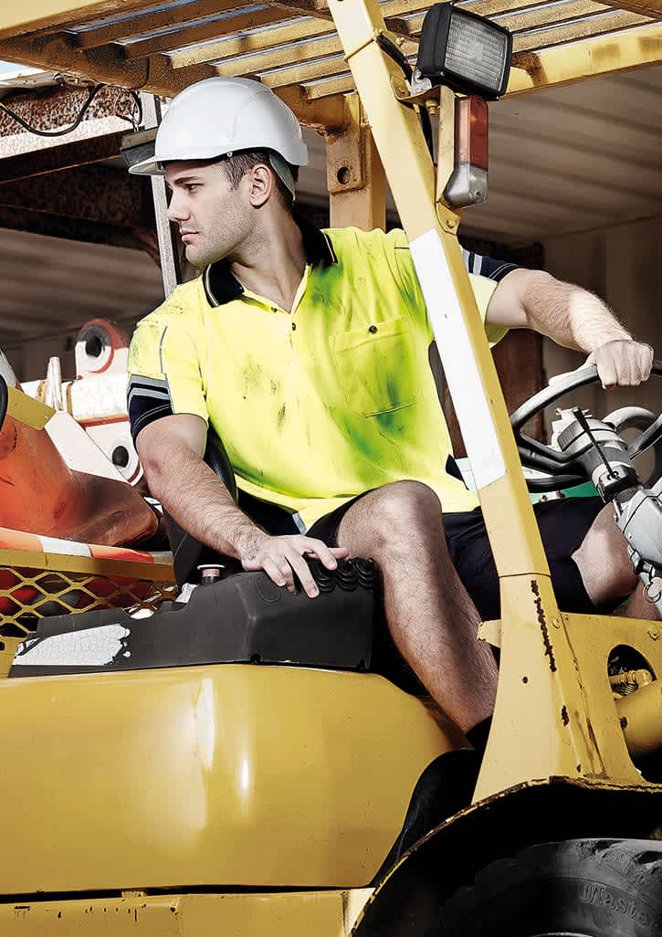 A man wearing a yellow and navy hi-vis short sleeve polo shirt operates a forklift, wearing a safety helmet.