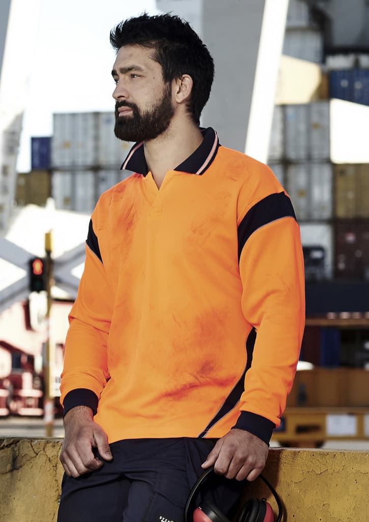 A long sleeve polo shirt in bright orange with navy accents, featuring a logo and worn by a man at a worksite.