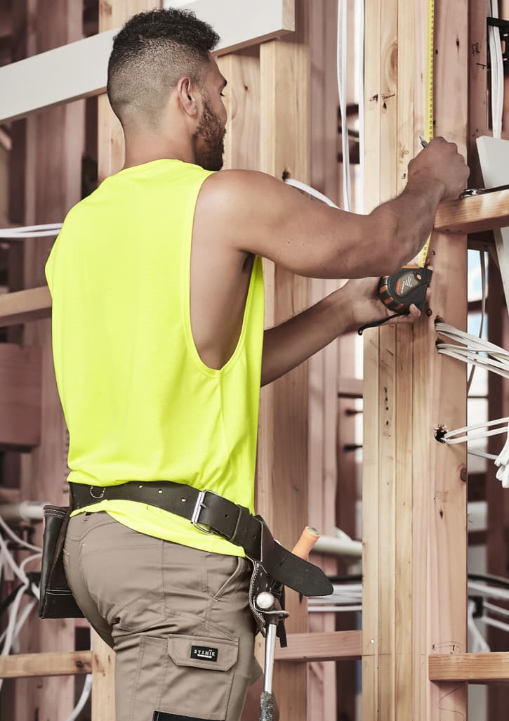 A man wearing a fluorescent yellow sleeveless tee is working with tools in a construction setting.