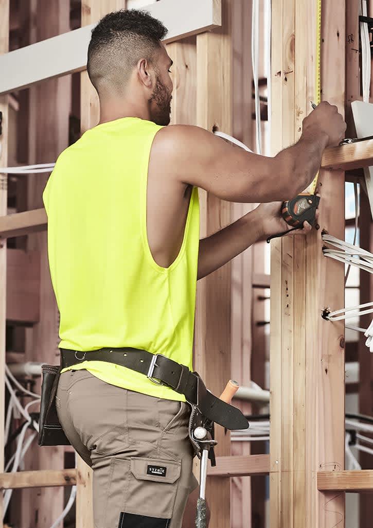A sleeveless high-visibility yellow tee worn by a man working on a construction site, measuring with a tool.