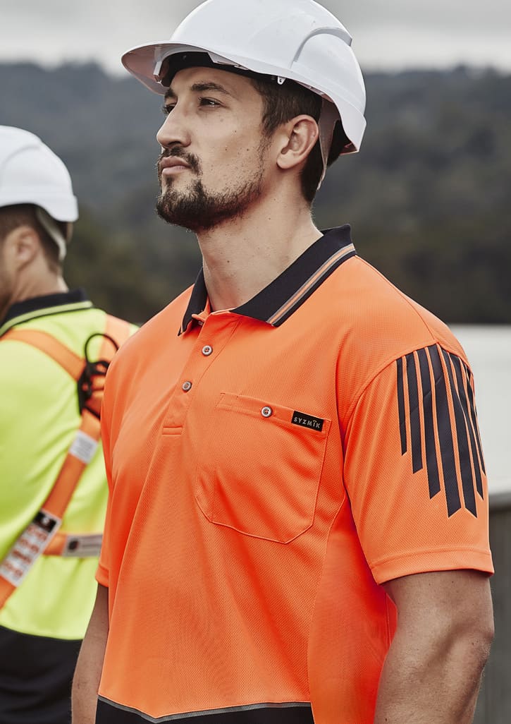 A man wearing an orange hi-vis short sleeve polo shirt with a pocket and a logo, paired with a safety helmet.