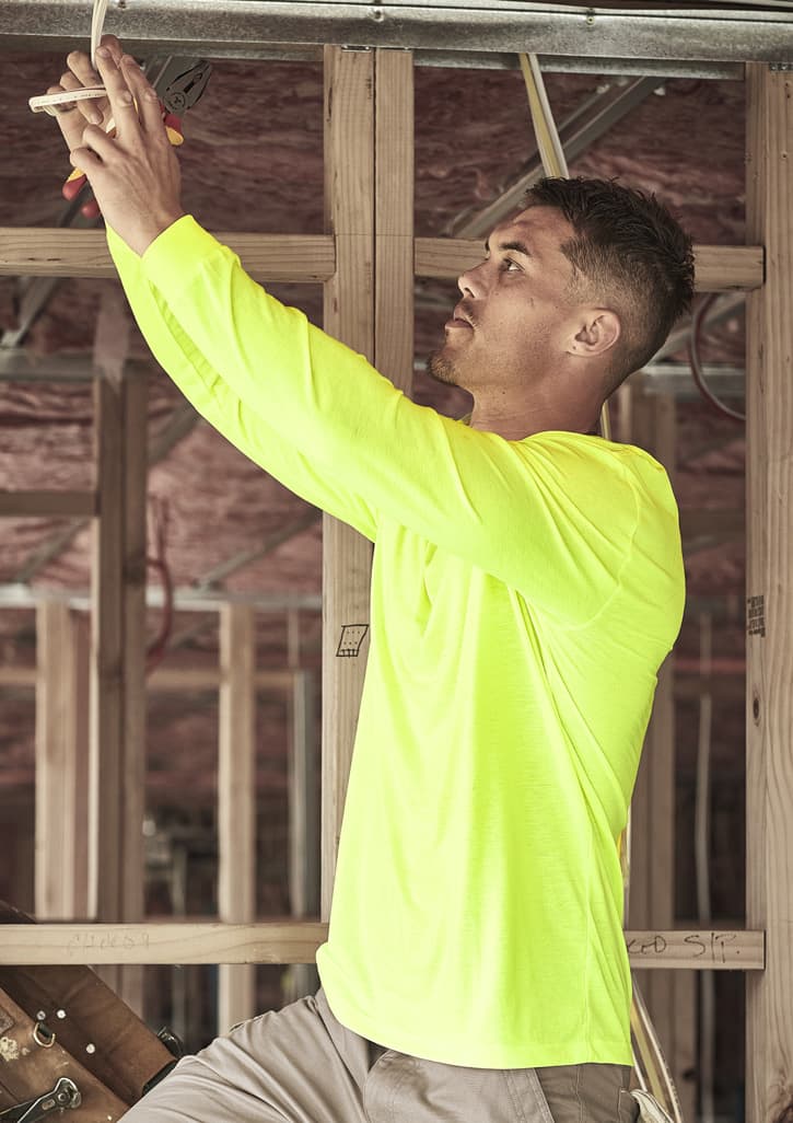 A man wearing a high visibility long sleeve tee in fluorescent yellow, working on electrical wiring in a construction setting.