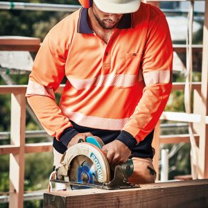 A worker in a high-visibility orange long-sleeve polo with reflective tape operates a circular saw on a construction site.