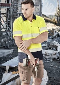 A unisex hi-vis segmented tape short sleeve polo in bright yellow and navy, featuring reflective stripes, held by a man on a worksite.