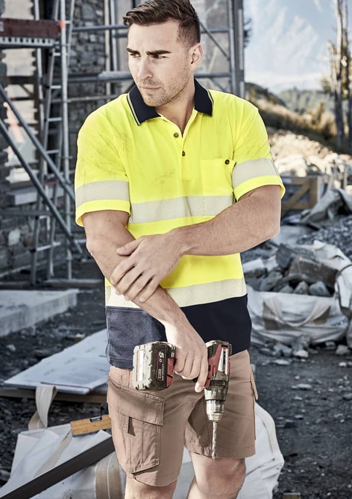 A unisex hi-vis segmented tape short sleeve polo in bright yellow and navy, featuring reflective stripes, held by a man on a worksite.