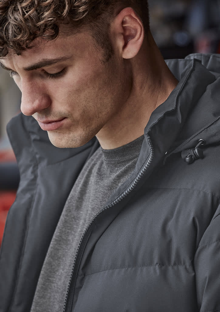 A close-up of a man wearing a dark grey hooded puffer jacket, featuring a zippered front and a casual look.