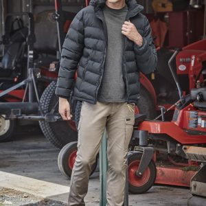 A black hooded puffer jacket is worn over a grey shirt, paired with beige pants and tan boots in an outdoor setting.