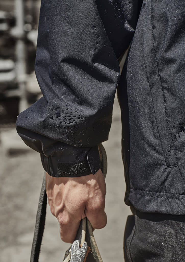 A close-up of a person's arm wearing a black packable rain jacket, holding a rope. The jacket features an adjustable cuff.