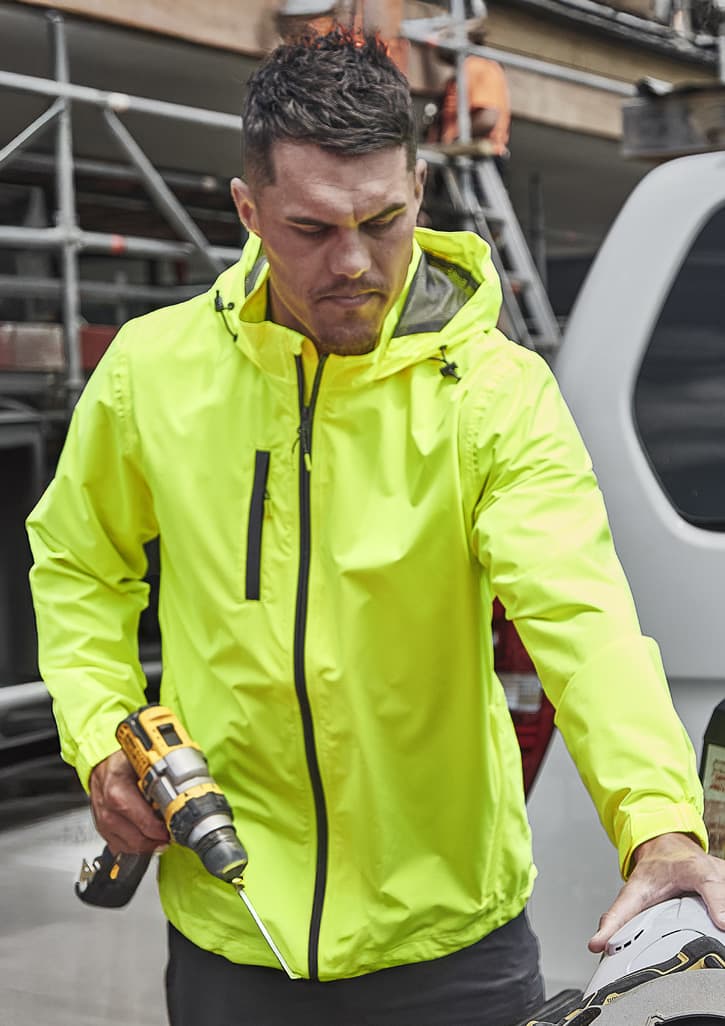 A man wearing a bright yellow unisex super light packable rain jacket, holding a drill and working outdoors.