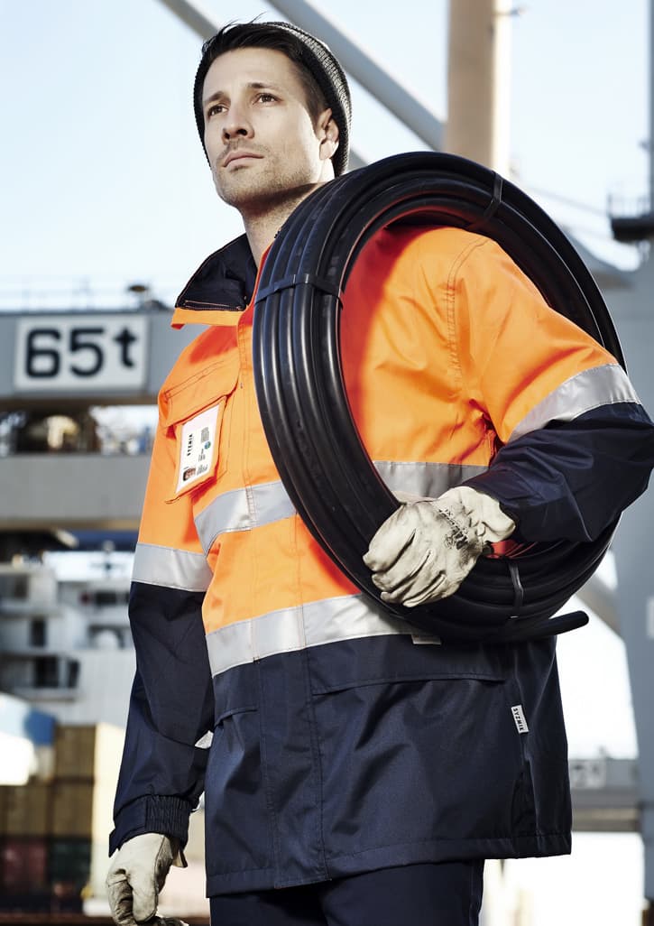 A man wearing an orange and navy waterproof jacket holds a coil of wire, showcasing a high-visibility workwear design.