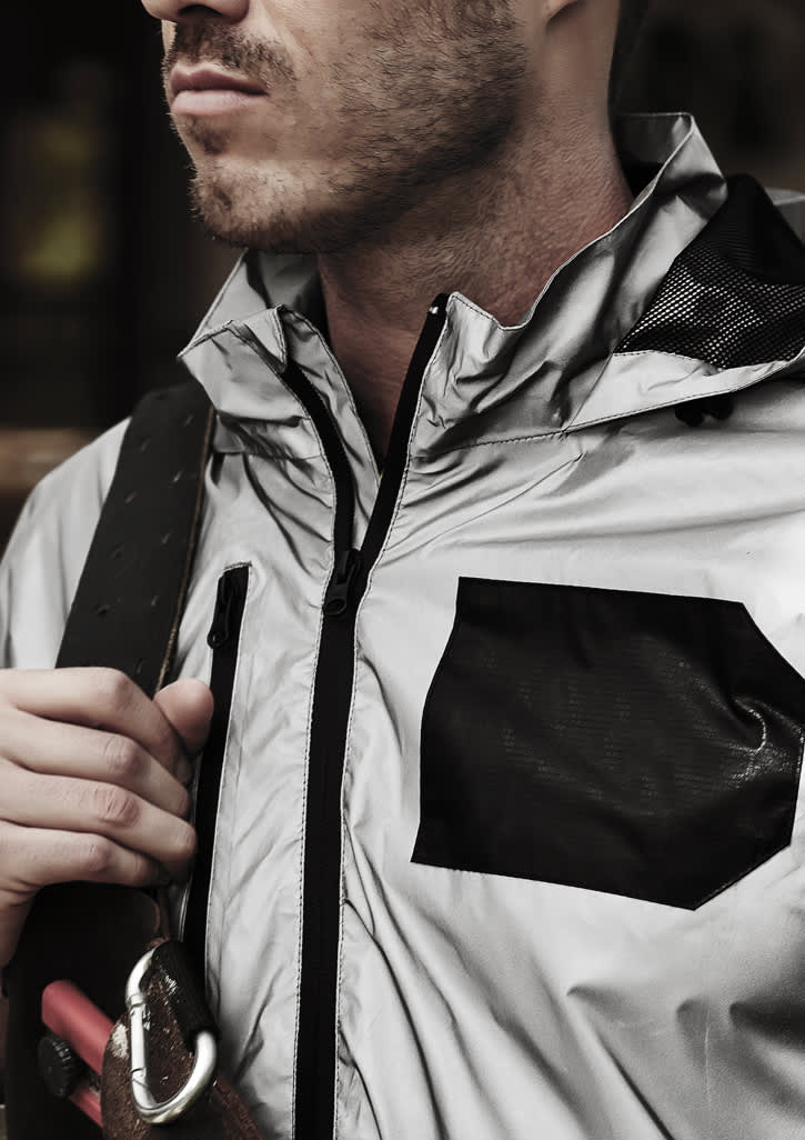 A reflective silver waterproof jacket with a black pocket, featuring a high collar and zip closure, worn by a model.
