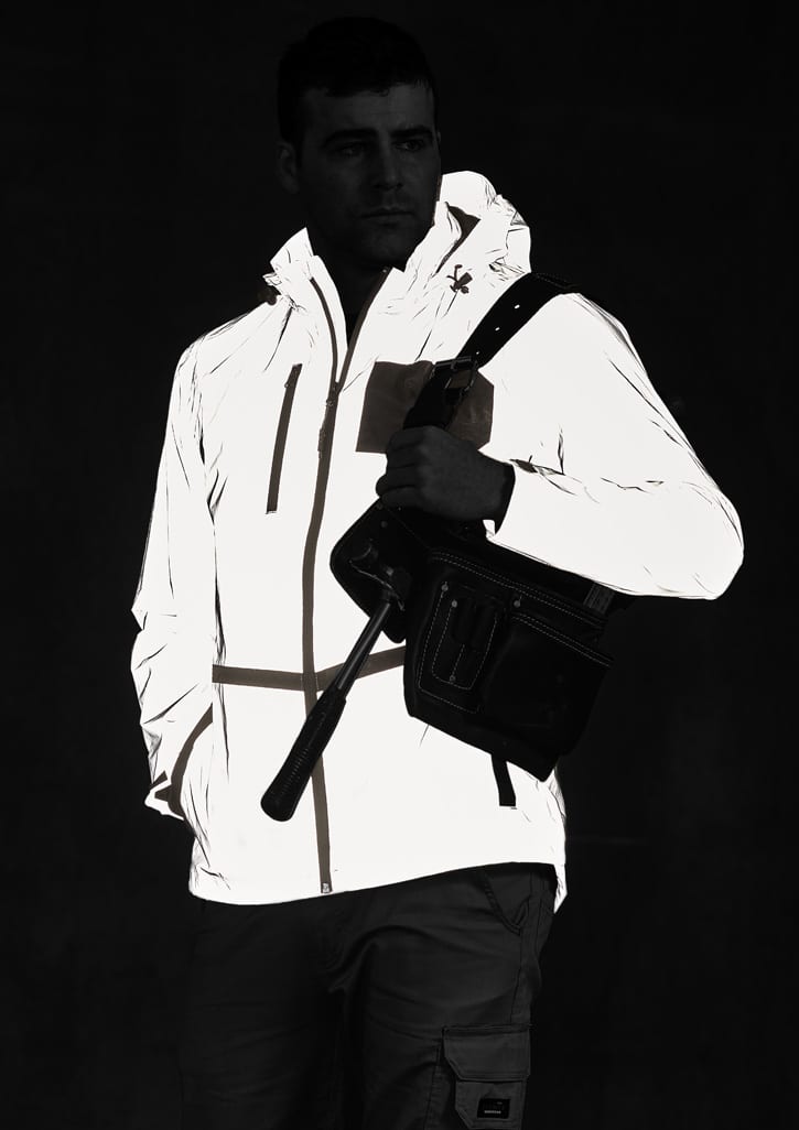 A reflective waterproof jacket in white, featuring a hood and pockets, worn by a model holding a bag.