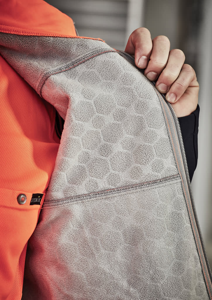 A close-up of an orange unisex softshell jacket showcasing a grey interior with a honeycomb texture and a zipper.