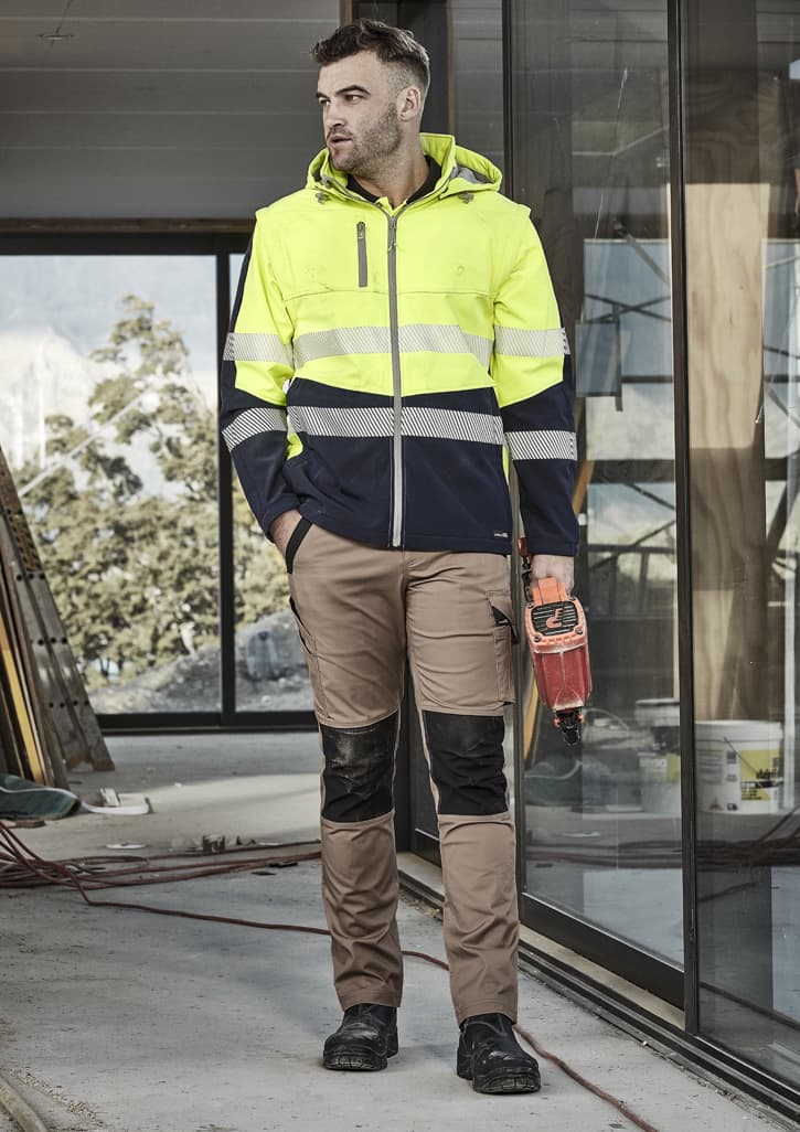 A man wearing a unisex two-tone softshell jacket in high visibility yellow and navy, paired with beige work trousers.