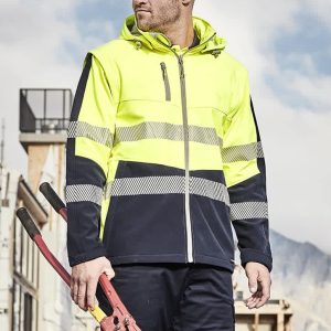 A man in a high-visibility yellow and navy softshell jacket holds red bolt cutters, set against a construction backdrop.