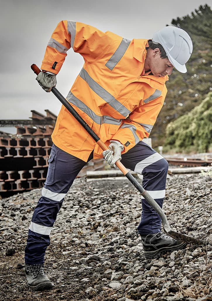 A waterproof orange jacket with reflective stripes, worn by a person digging with a spade, set in an outdoor work environment.