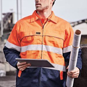 A man wearing a men's hi-vis cotton drill jacket in orange and navy, holding a blueprint and wearing a helmet.