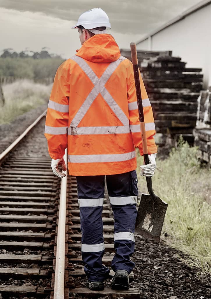 An orange waterproof jacket with reflective stripes, worn by a person holding a shovel, walking along railway tracks.