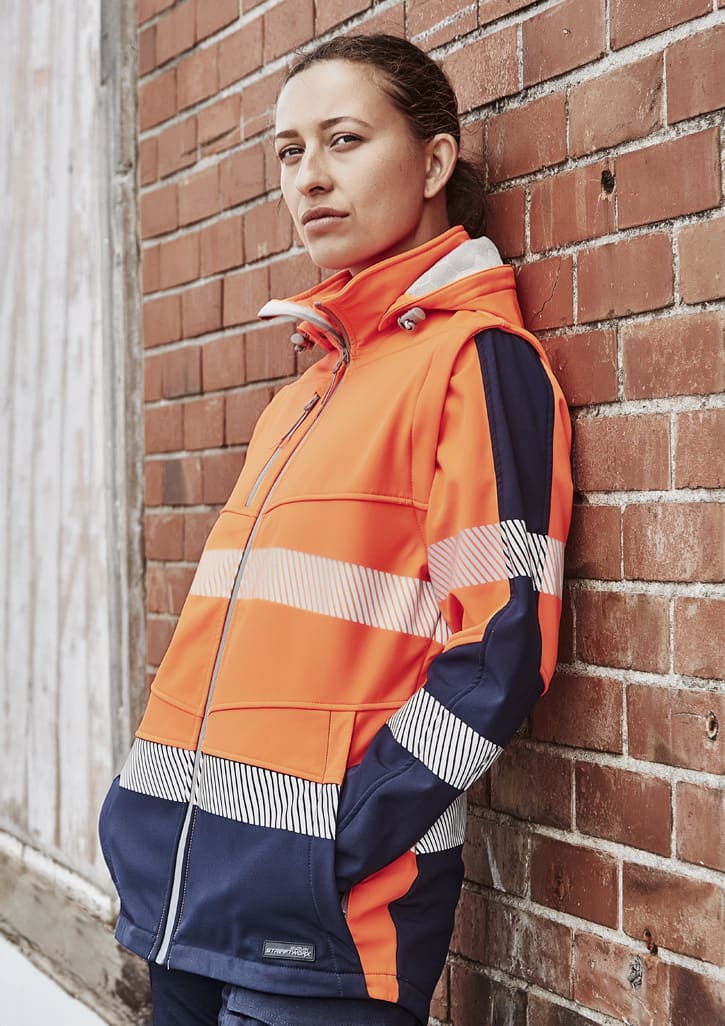 A women's softshell jacket in bright orange and navy, featuring reflective strips and a logo.