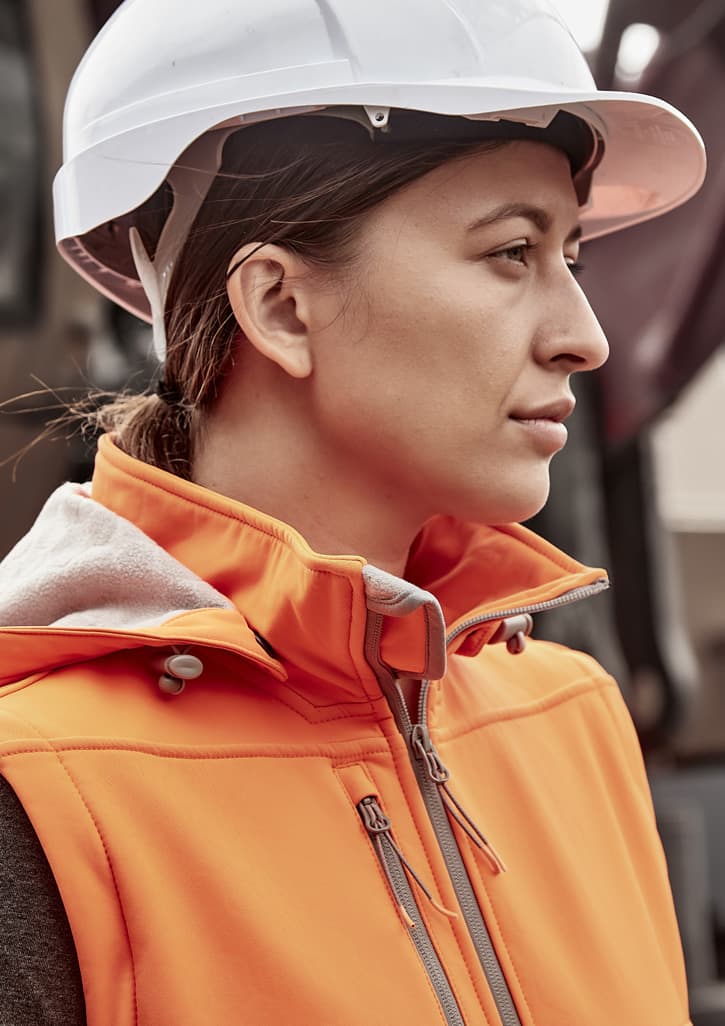 An orange women's softshell jacket with a zipper, worn by a woman in a white hard hat.