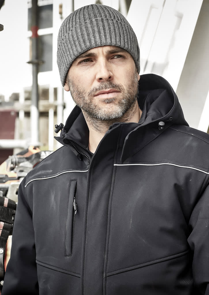 A grey beanie worn by a man in a black jacket, with an industrial background. The beanie features a logo.