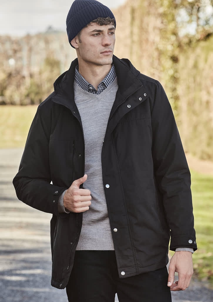 A model wearing a black jacket and a navy beanie, standing outdoors with greenery in the background.