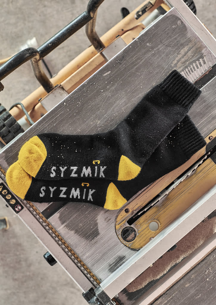 A pair of black work socks with yellow accents, featuring branding, displayed on a metallic surface.