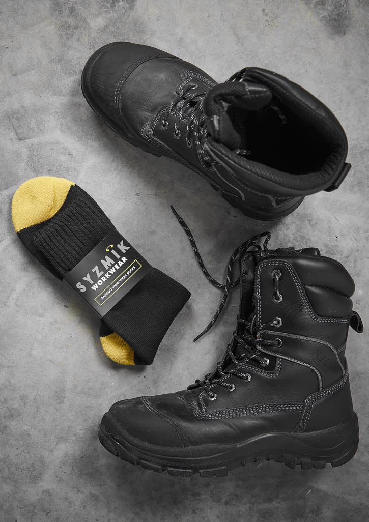 A pair of black work boots with yellow and black socks in between. The socks have a logo on the packaging.