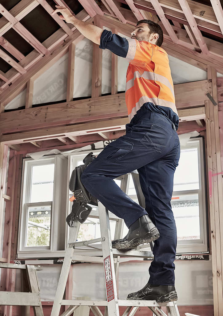 Men's cargo pant in navy, worn by a man on a ladder, working in a partially constructed building. The pants have pockets and a logo.