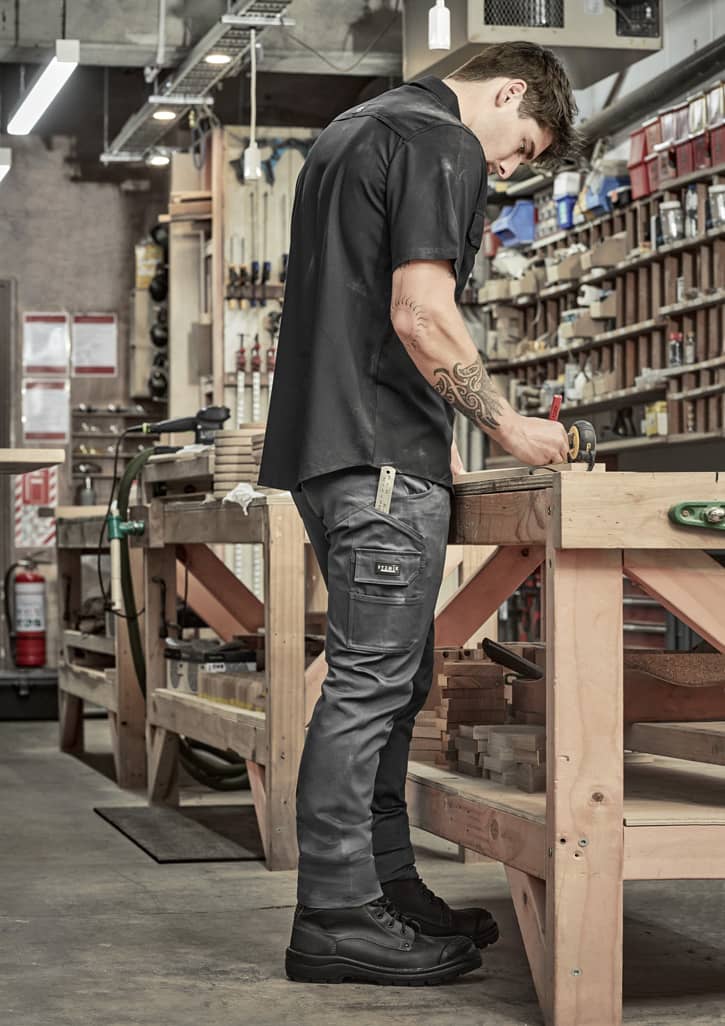 Men's essential basic stretch cargo pants in grey, featuring pockets and a logo, worn by a person in a workshop setting.