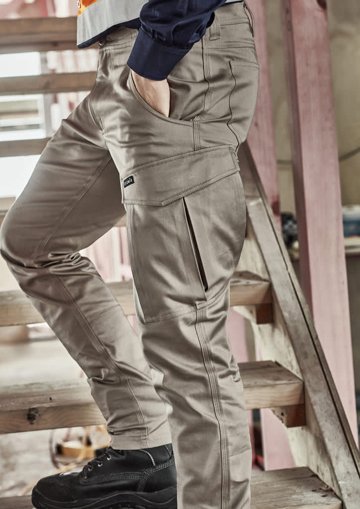A model wearing beige cargo pants, featuring multiple pockets, standing on a wooden staircase.