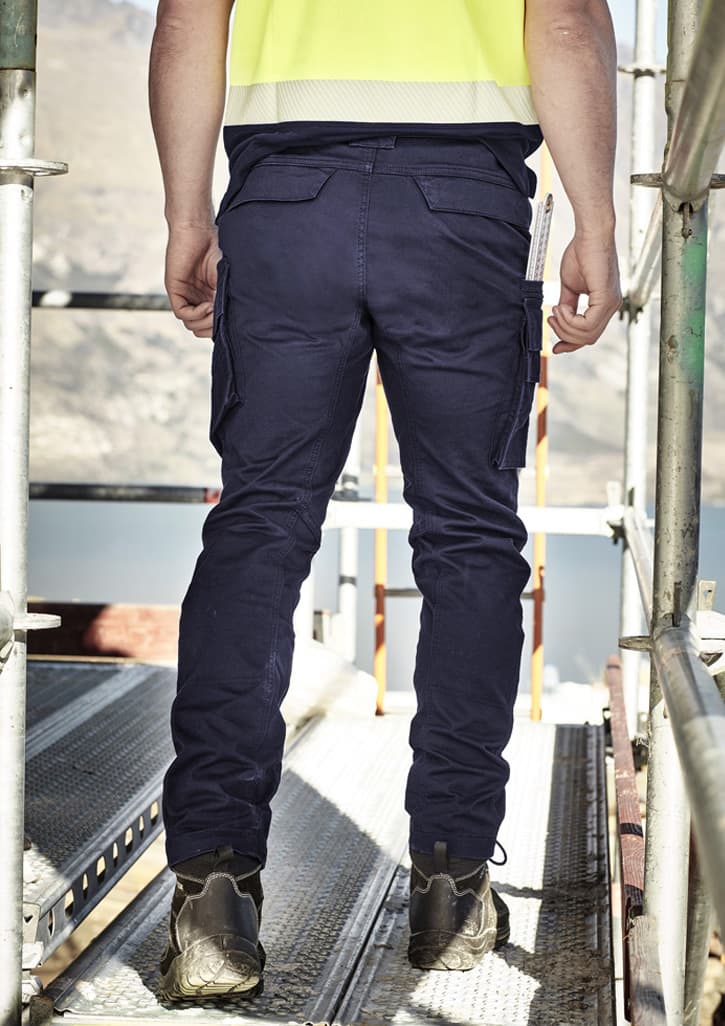 Men's curved cargo pants in navy blue, featuring multiple pockets and a fitted design, set against a construction backdrop.