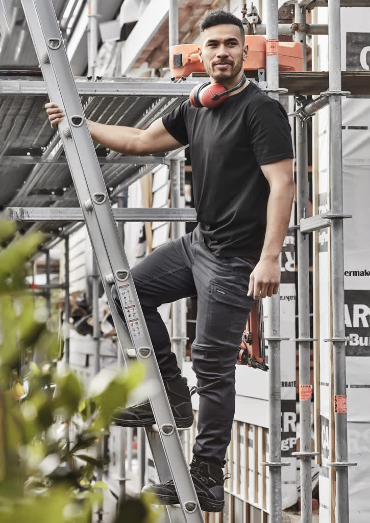 Men's streetwear comfort pants in black, displayed on a model climbing a ladder at a construction site.
