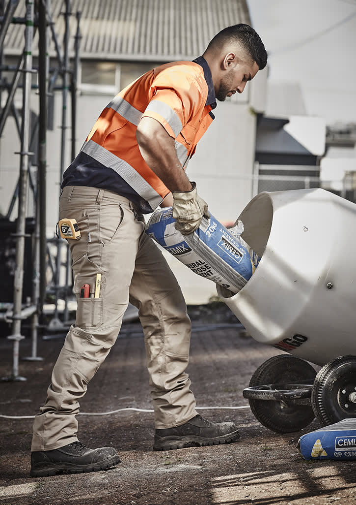 Men’s cargo pants in beige, featuring multiple pockets, worn by a worker pouring materials into a mixer.