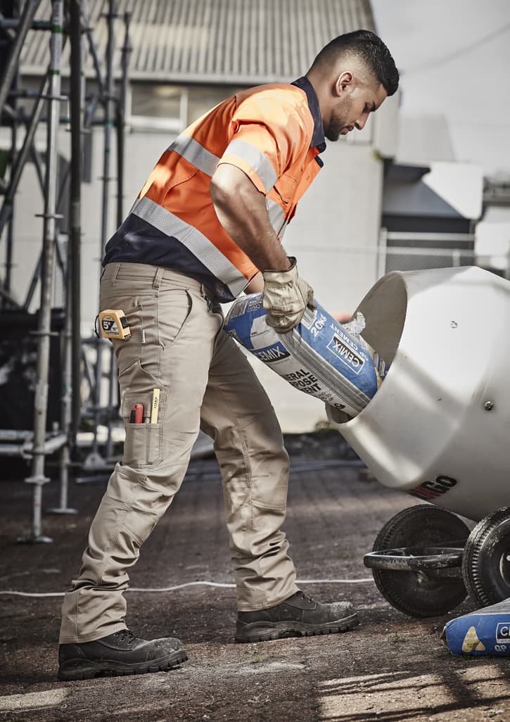 Men’s rugged cargo pants in beige, featuring multiple pockets, worn with an orange high-visibility shirt and black boots.