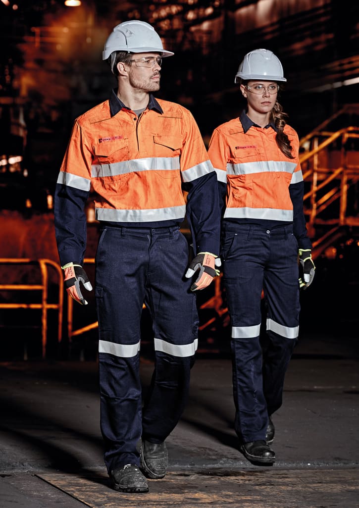 Two individuals in high-visibility orange shirts with reflective strips and navy cargo pants, wearing safety helmets and gloves.
