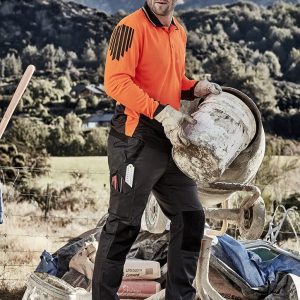 A worker in an orange high-visibility shirt and black tough pants, holding a bucket on a job site with mountains in the background.