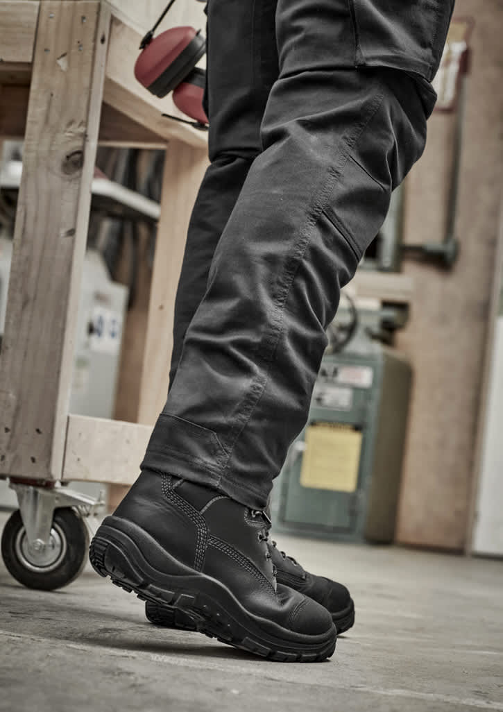 A pair of black rugged cooling stretch pants paired with black boots, set in an industrial environment.